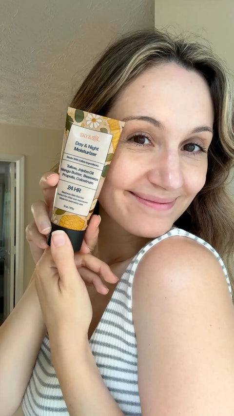 Smiling woman holding a tube of The Everything Cream next to her cheek