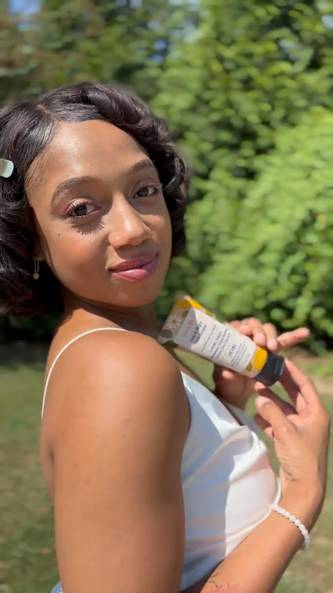 Woman outdoors holding The Everything Cream tube near her shoulder