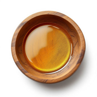 Wooden bowl of glossy golden jojoba oil